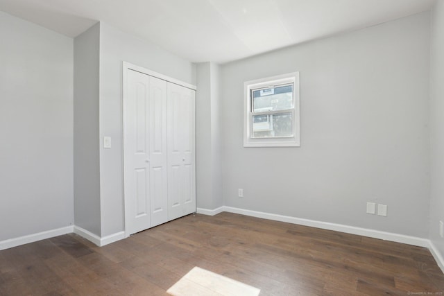 unfurnished bedroom featuring a closet, dark wood finished floors, and baseboards