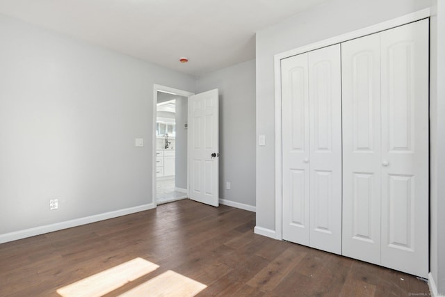 unfurnished bedroom with baseboards, dark wood finished floors, and a closet