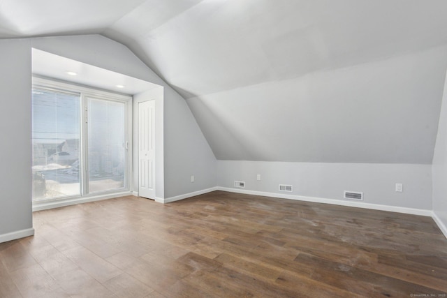 additional living space featuring dark wood-style floors, lofted ceiling, visible vents, and baseboards