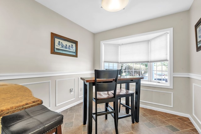 dining area with a wainscoted wall, stone finish floor, and a decorative wall