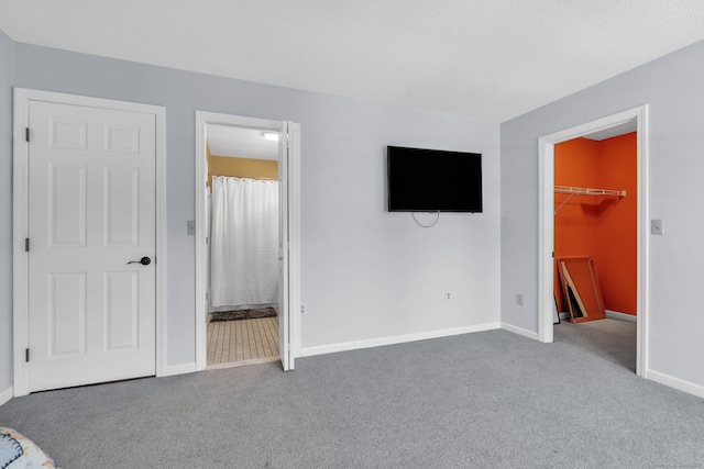 unfurnished bedroom featuring ensuite bath, carpet, a walk in closet, and baseboards