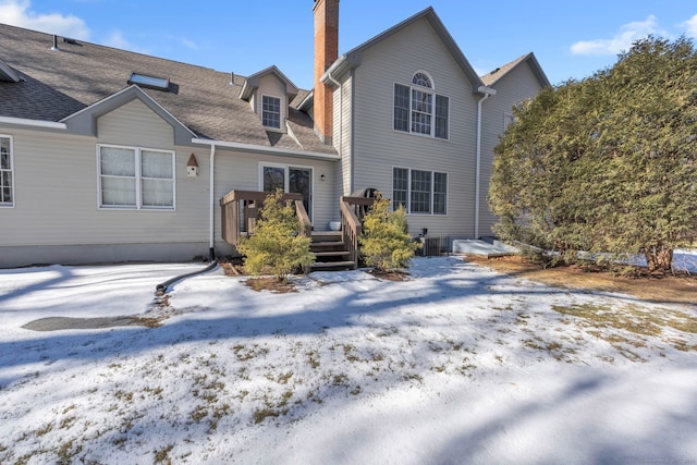 snow covered back of property with a chimney, a deck, and roof with shingles