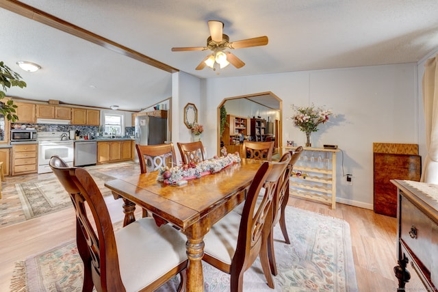 dining area with lofted ceiling, light wood finished floors, arched walkways, and a ceiling fan