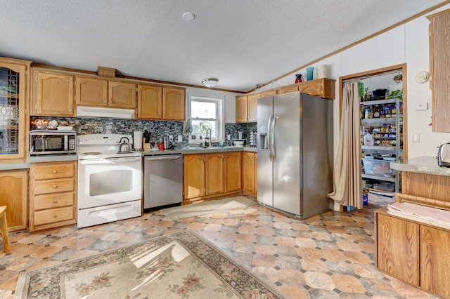 kitchen featuring appliances with stainless steel finishes, vaulted ceiling, light countertops, under cabinet range hood, and a sink