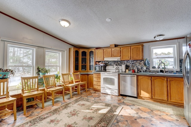 kitchen with brown cabinets, stainless steel appliances, lofted ceiling, stone finish floor, and under cabinet range hood