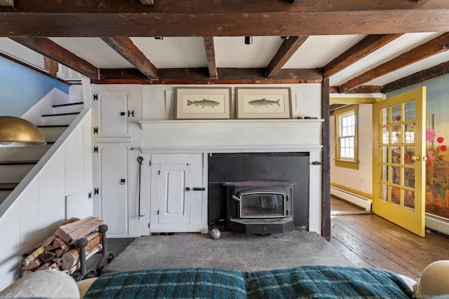 unfurnished living room featuring stairs, beam ceiling, a baseboard heating unit, a wood stove, and hardwood / wood-style flooring