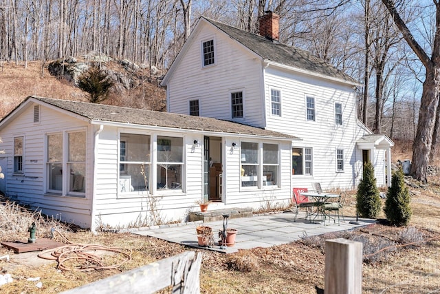 view of front of home with a chimney, a patio, and roof with shingles