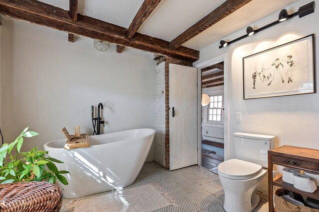 full bathroom featuring toilet, tile patterned flooring, a freestanding bath, and beam ceiling