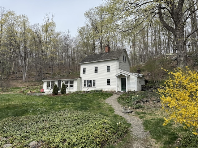 view of front facade with a chimney, a shingled roof, and a front lawn
