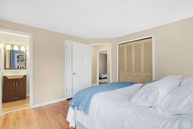 bedroom with a closet, connected bathroom, light wood-type flooring, and baseboards