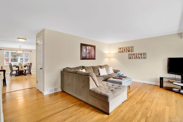 living room with light wood finished floors, visible vents, a chandelier, and baseboards