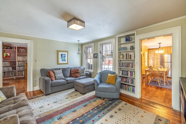 living area with baseboards, an inviting chandelier, ornamental molding, and hardwood / wood-style floors
