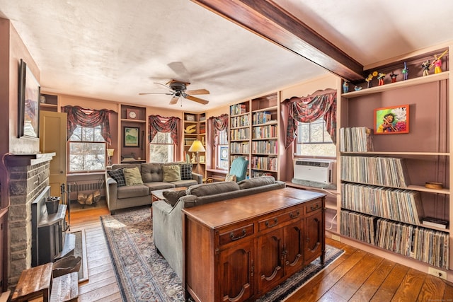 living room featuring wood-type flooring, beamed ceiling, ceiling fan, a fireplace with raised hearth, and cooling unit