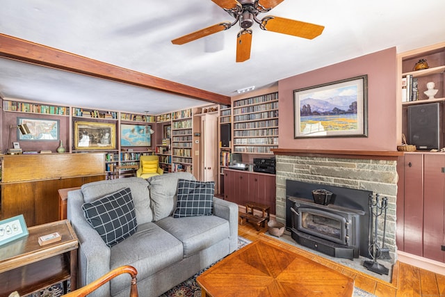 living area with a wood stove, built in shelves, a ceiling fan, wood finished floors, and beamed ceiling