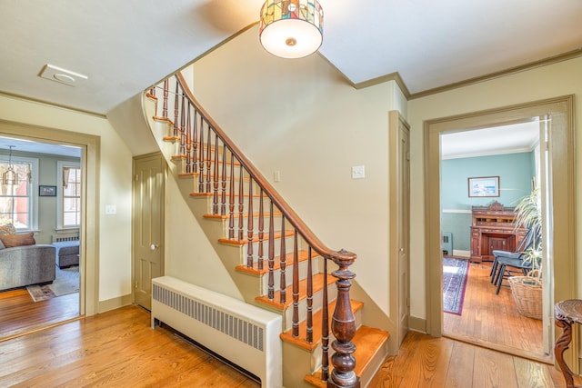 staircase featuring radiator, ornamental molding, wood-type flooring, and a fireplace with raised hearth