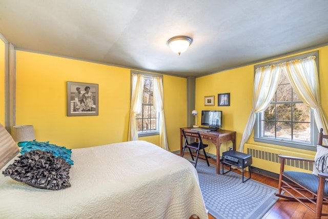 bedroom featuring radiator heating unit, baseboards, and wood finished floors