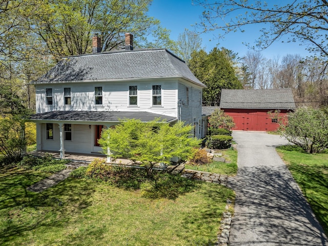 view of front of house featuring covered porch, aphalt driveway, a front yard, a chimney, and an outdoor structure