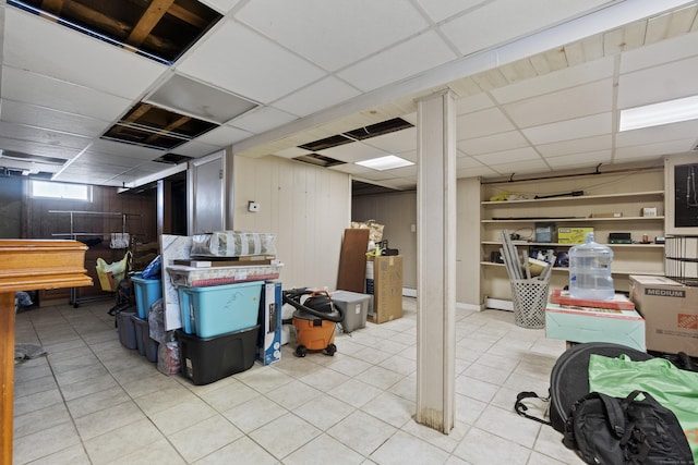 basement featuring a paneled ceiling, light tile patterned floors, a baseboard radiator, and wood walls