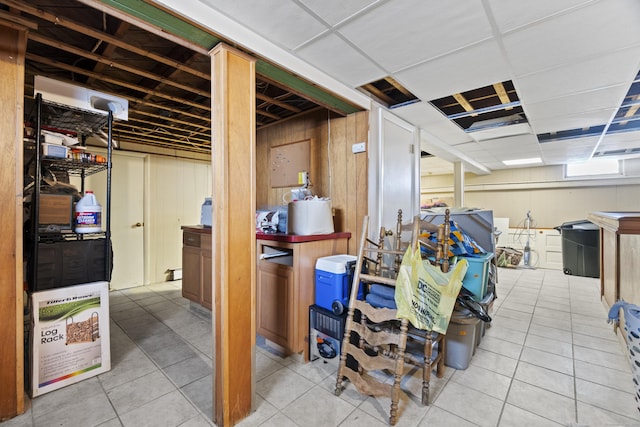 finished basement with light tile patterned flooring, a paneled ceiling, and wooden walls