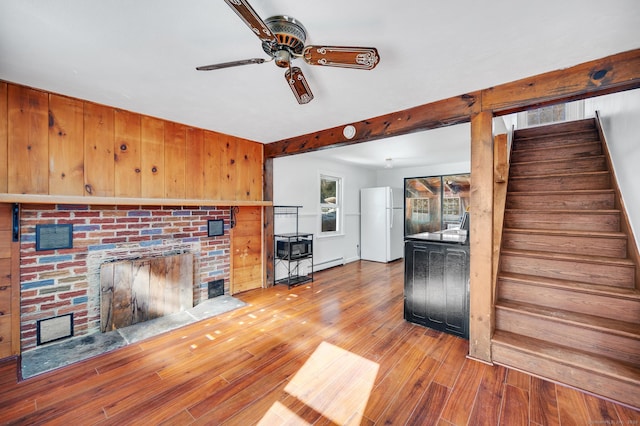 unfurnished living room featuring hardwood / wood-style floors, ceiling fan, stairs, a brick fireplace, and baseboard heating