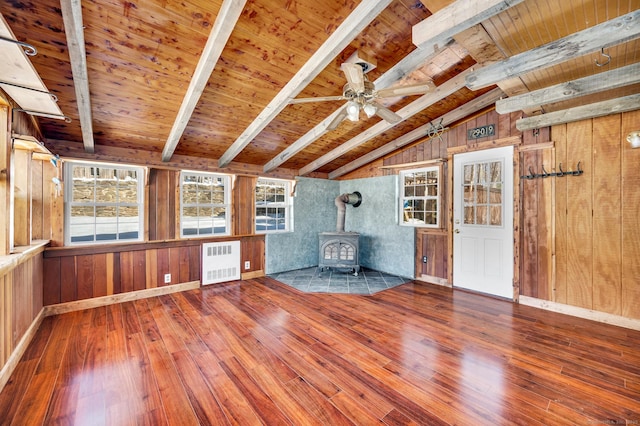 interior space with lofted ceiling with beams, wood finished floors, radiator, wooden ceiling, and a wood stove