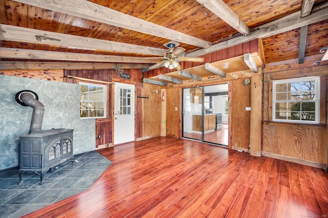 unfurnished living room featuring beam ceiling, a wood stove, wooden walls, and wood ceiling