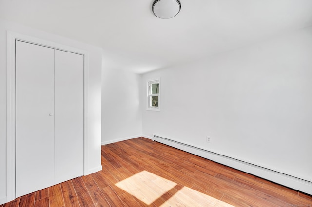 unfurnished bedroom with a baseboard heating unit, wood finished floors, a closet, and baseboards