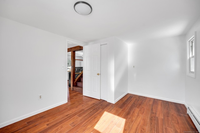 spare room with baseboard heating, stairs, baseboards, and wood finished floors