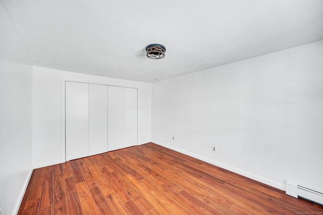 unfurnished bedroom featuring a closet, wood-type flooring, baseboard heating, and baseboards