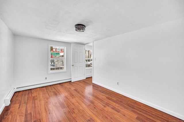 spare room with a textured ceiling, wood finished floors, baseboards, and a baseboard radiator