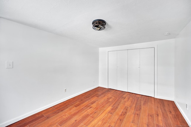 unfurnished bedroom featuring a closet, a textured ceiling, baseboards, and light wood-style floors