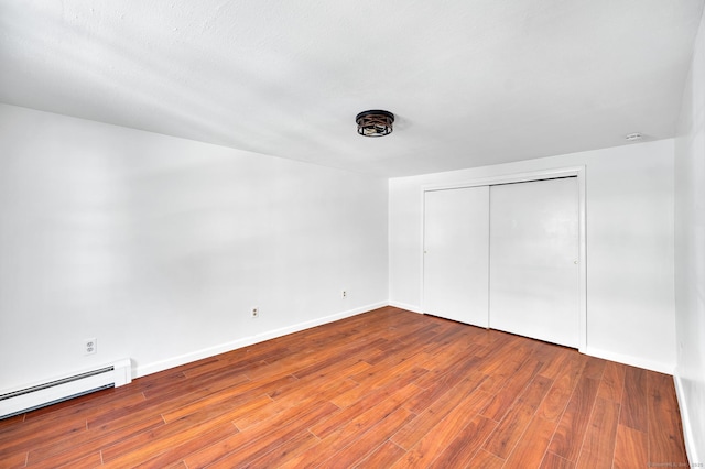 unfurnished bedroom featuring a baseboard heating unit, baseboards, a closet, and wood finished floors