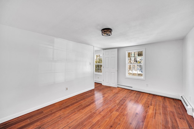 empty room with baseboards, baseboard heating, and wood finished floors