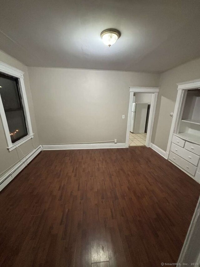 unfurnished bedroom featuring a baseboard heating unit, freestanding refrigerator, baseboards, and wood finished floors