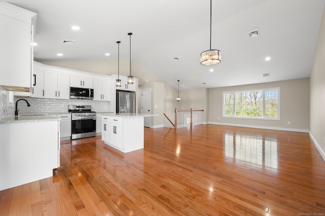 kitchen with visible vents, a sink, open floor plan, stainless steel appliances, and decorative backsplash