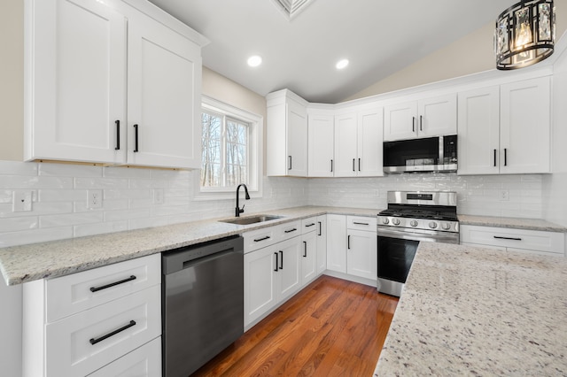 kitchen with vaulted ceiling, stainless steel appliances, wood finished floors, white cabinetry, and a sink