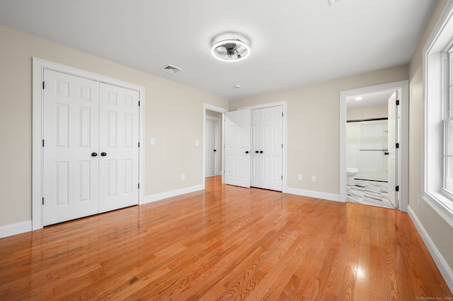 unfurnished bedroom with light wood finished floors, baseboards, visible vents, and two closets