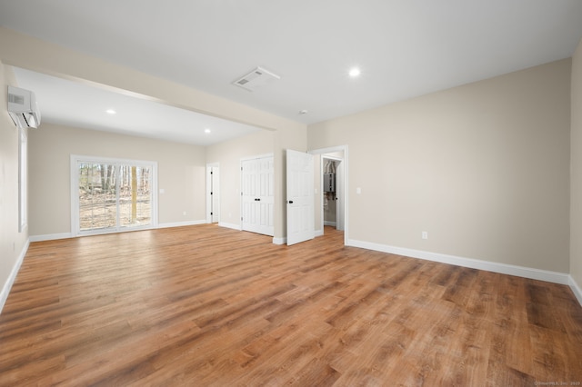 unfurnished room with visible vents, baseboards, light wood-type flooring, a wall unit AC, and recessed lighting