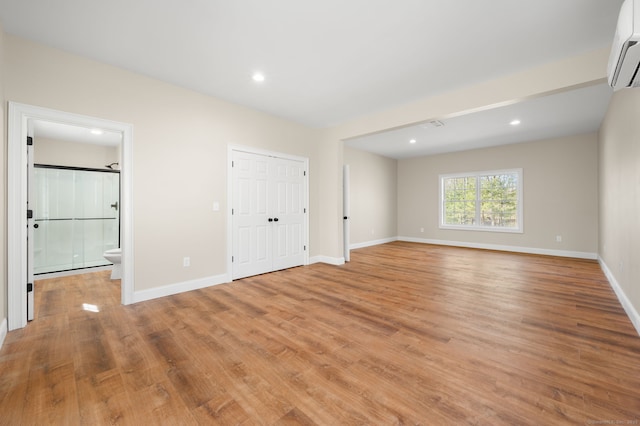 empty room featuring recessed lighting, light wood-style flooring, an AC wall unit, and baseboards