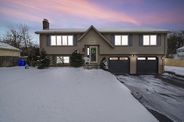 bi-level home featuring an attached garage, a chimney, and fence