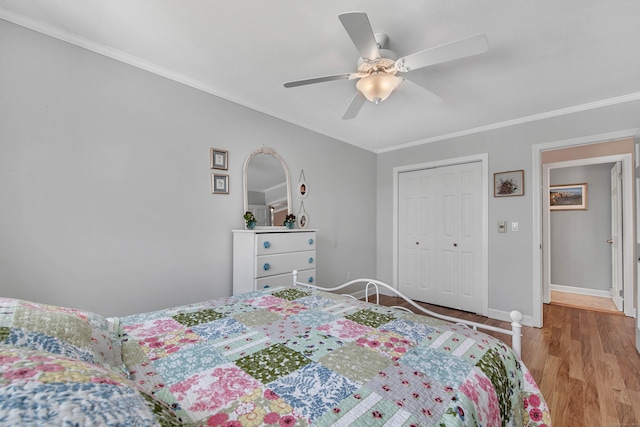 bedroom with ceiling fan, wood finished floors, baseboards, ornamental molding, and a closet