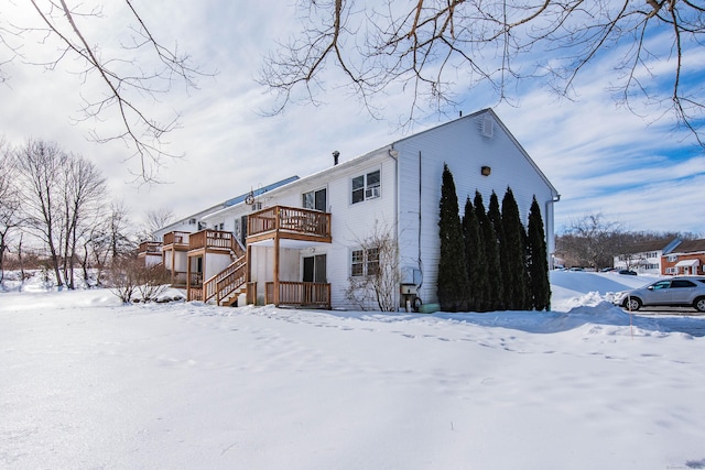 snow covered house with a deck, stairway, and a balcony