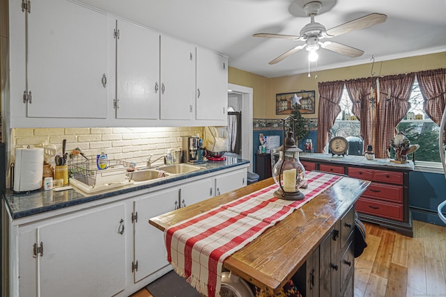 kitchen with dark countertops, decorative backsplash, a ceiling fan, white cabinets, and light wood-type flooring