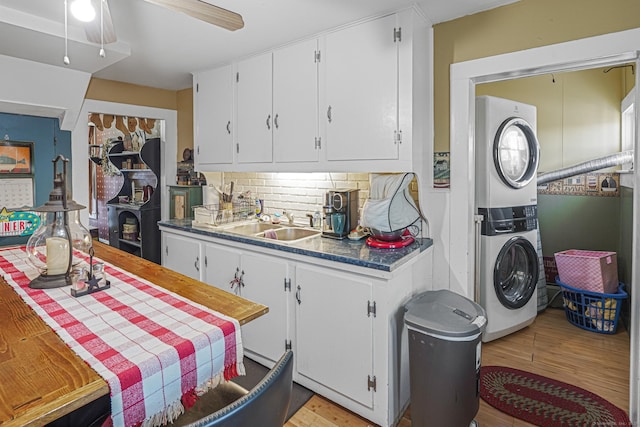 kitchen with tasteful backsplash, dark countertops, white cabinets, stacked washing maching and dryer, and light wood-type flooring