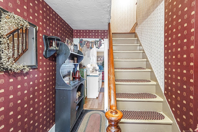 stairway with a textured ceiling, wood finished floors, and wallpapered walls