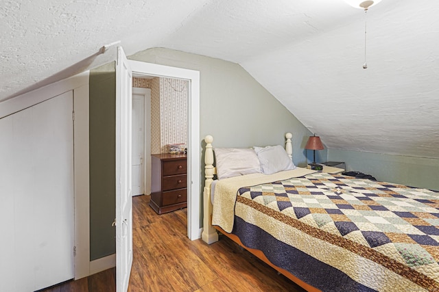 bedroom featuring a textured ceiling, baseboards, wood finished floors, and lofted ceiling