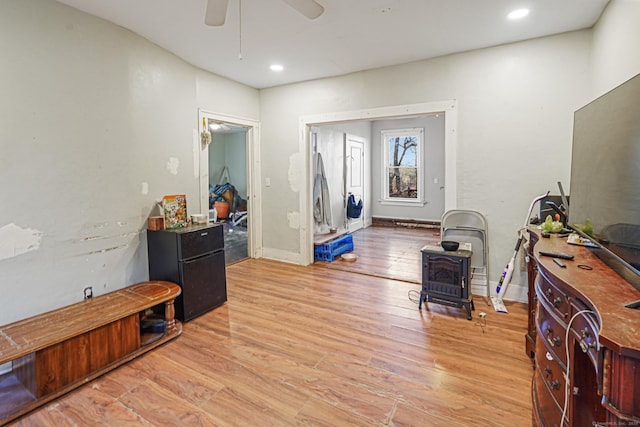 interior space with baseboards, a ceiling fan, a wood stove, light wood-style floors, and recessed lighting