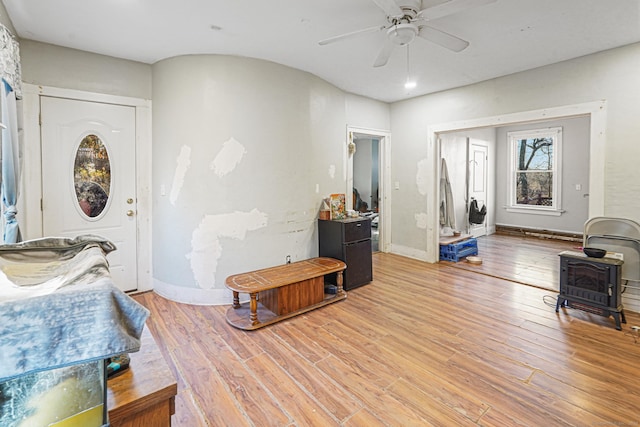 foyer featuring light wood-style floors, a wood stove, baseboards, and a ceiling fan