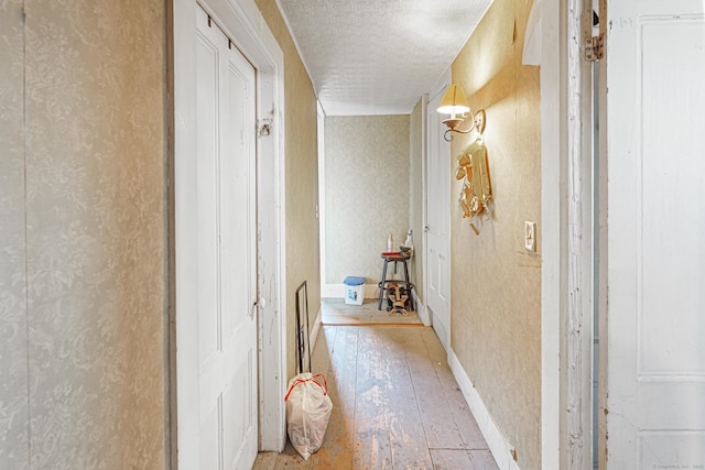 hallway with wallpapered walls, light wood-style flooring, and a textured ceiling