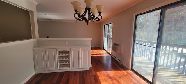 unfurnished dining area featuring crown molding, wood finished floors, baseboards, an AC wall unit, and an inviting chandelier